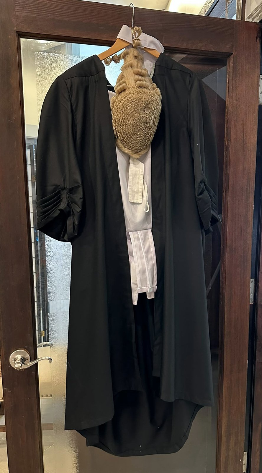 A barrister's wig and black gown hanging on a wooden office door